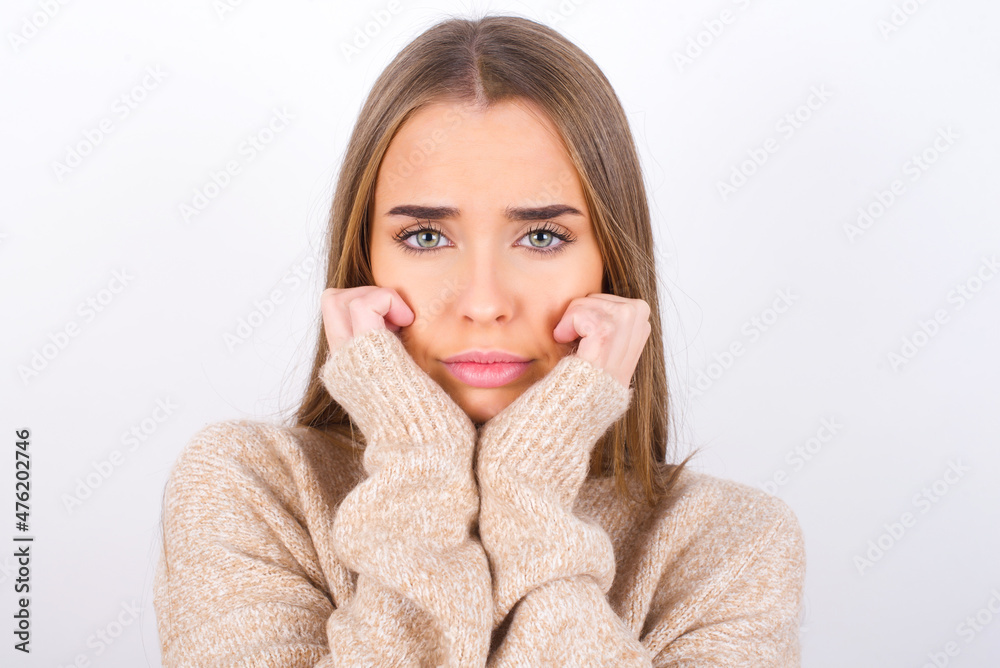 Portrait of sad young caucasian girl wearing knitted sweater over white background hands face Portrait of sad young caucasian girl wearing knitted sweater over white background hands face