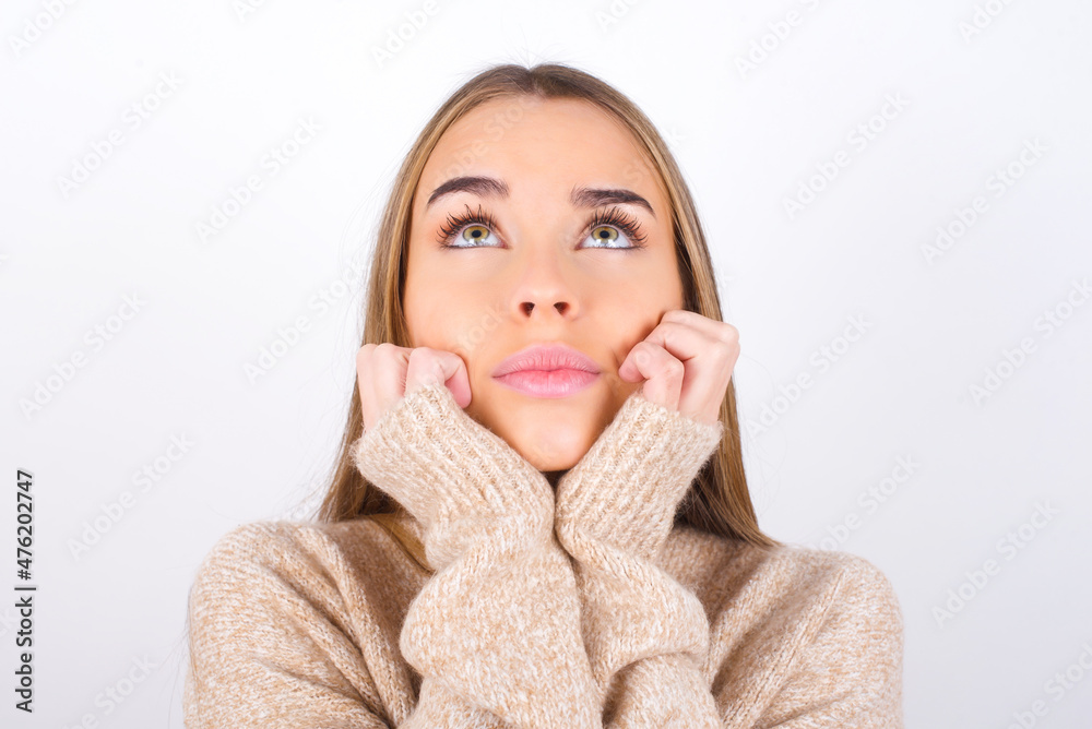 Portrait of sad young caucasian girl wearing knitted sweater over white background hands face look empty space Portrait of sad young caucasian girl wearing knitted sweater over white background hands face look empty space