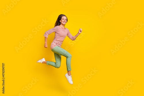 Photo of adorable shiny young woman wear striped shirt smiling jumping high running fast empty space isolated yellow color background