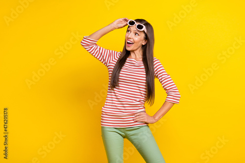 Photo of impressed funky mature lady dressed striped shirt arm dark eyewear looking empty space smiling isolated yellow color background