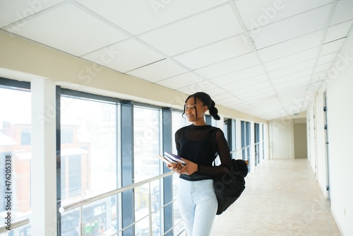 Pretty afro american female student with backpack and paperwork at classroom of university