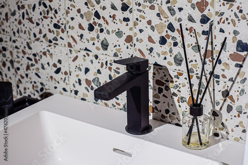 Black faucet on the washbasin in the bathroom, the wall is decorated with terrazzo-style tiles