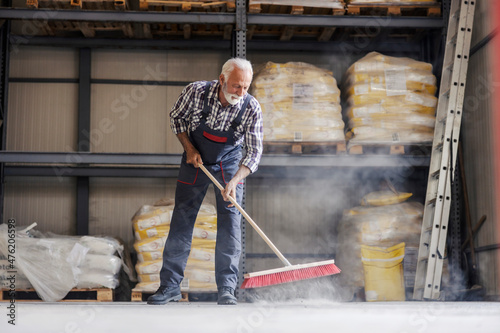 Billede på lærred A senior worker is cleaning a factory with a broom