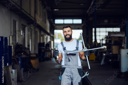 An auto-mechanic is standing in his workshop and holding tools. He is ready to repair trucks, cars, and buses. Worker in the auto-mechanic workshop