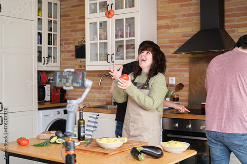 Young woman juggling with tomatoes and recording a video with her smartphone. photo