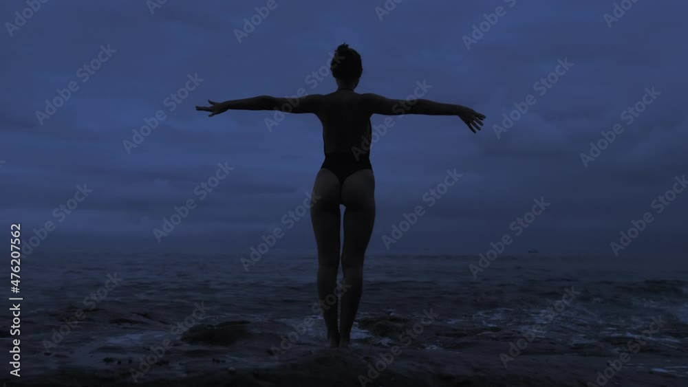 Happy slender women stands on stone ocean beach and up her hands. Twilight light Happy slender women stands on stone ocean beach and up her hands. Twilight light