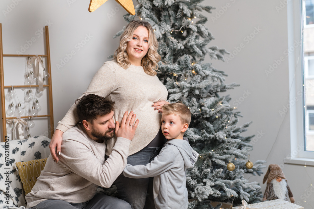 Christmas Family Happiness Portrait of dad, pregnant mom and little son  sitting armchair at home near Christmas tree hug smile