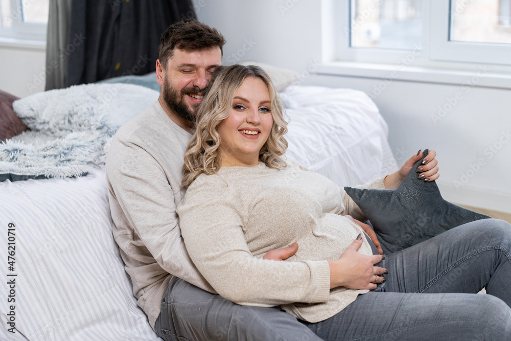 Happy family concept. Husband hug belly pregnant wife sitting floor indoor living room near sofa