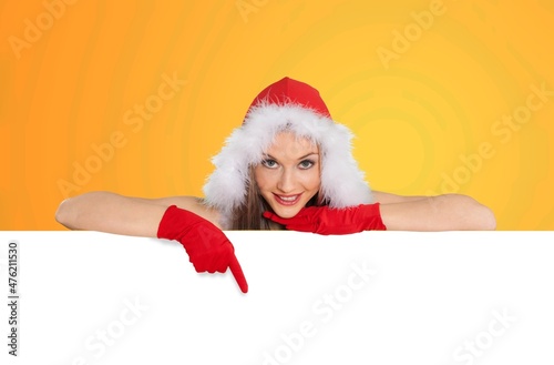 Christmas Happy woman In Santa Hat Pointing At White Advertisement Board With Hand. © BillionPhotos.com