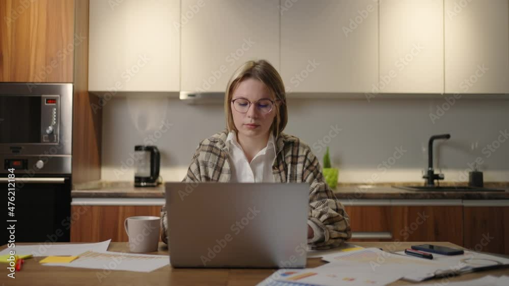 Zoom camera A woman with glasses works remotely from home sitting at a table with a laptop and a felt-tip pen marks the data on the graph. Distance learning student at home to perform an assignment Zoom camera A woman with glasses works remotely from home sitting at a table with a laptop and a felt-tip pen marks the data on the graph. Distance learning student at home to perform an assignment
