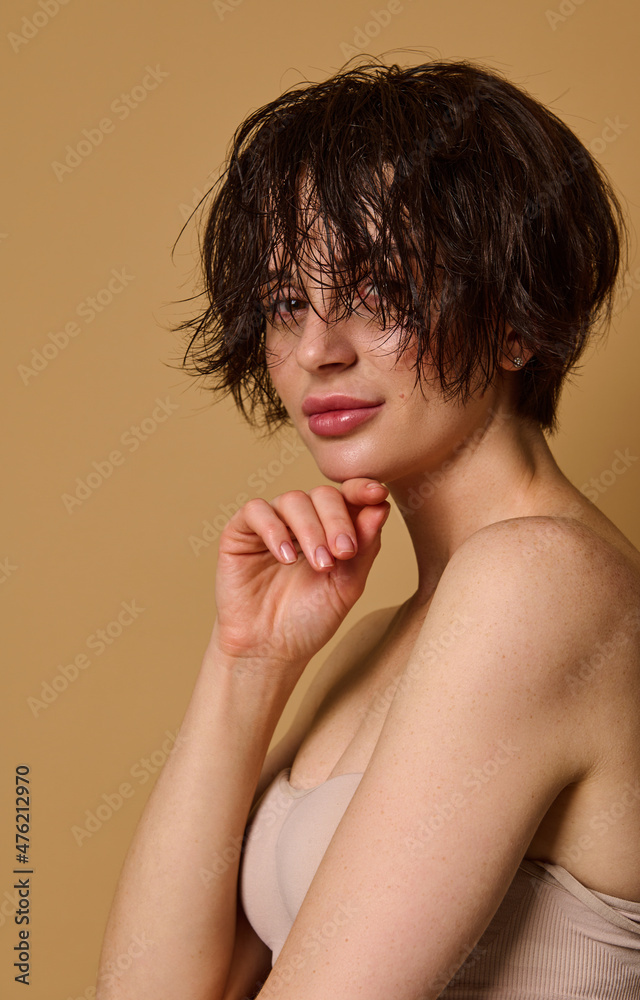 Obraz premium Beautiful attractive young European woman with wet short hair and perfect nude make-up, clean fresh healthy skin, wearing a beige underwear, posing against beige background with copy ad space