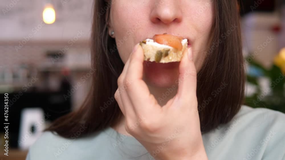 Woman takes a bite of a salmon sandwich made from whole wheat bread with sunflower and pumpkin seeds. Woman takes a bite of a salmon sandwich made from whole wheat bread with sunflower and pumpkin seeds.