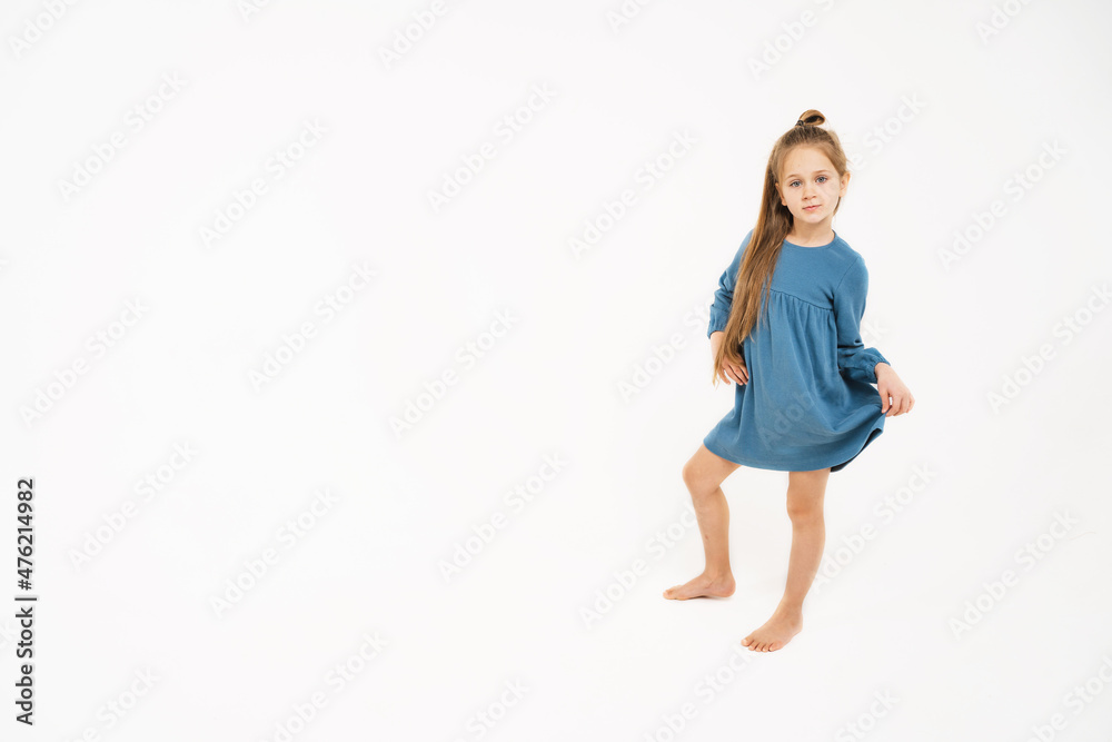 Cute little girl in a blue dress. A place for text and advertising. A beautiful child with long blonde hair. A girl in full growth on a monochromatic background.