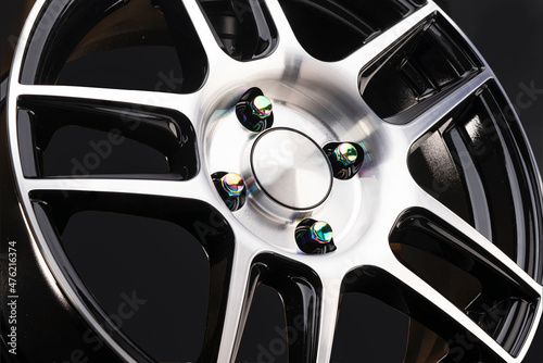 sporty lightweight alloy wheel with thin beams spokes and rim, with beautiful chameleon nuts of rainbow multicolored color on a black background