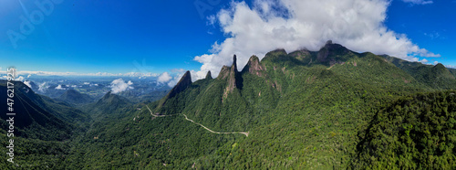 Wide aerial panorama landscape of road meandering through postcard trail Brazilian mountain range Serra dos Orgaos in Teresopolis, Rio de Janeiro, with Finger of God peak against blue sky with clouds photo