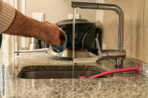 Man washing a cup and dishes in the kitchen sink. Concept of gender equality in household chores..