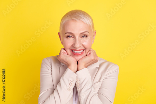 Photo of attractive aged woman good mood arms touch chin good mood isolated over yellow color background photo