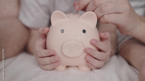 Foto little child with mother and father throw coins of money at pig, happy family sa