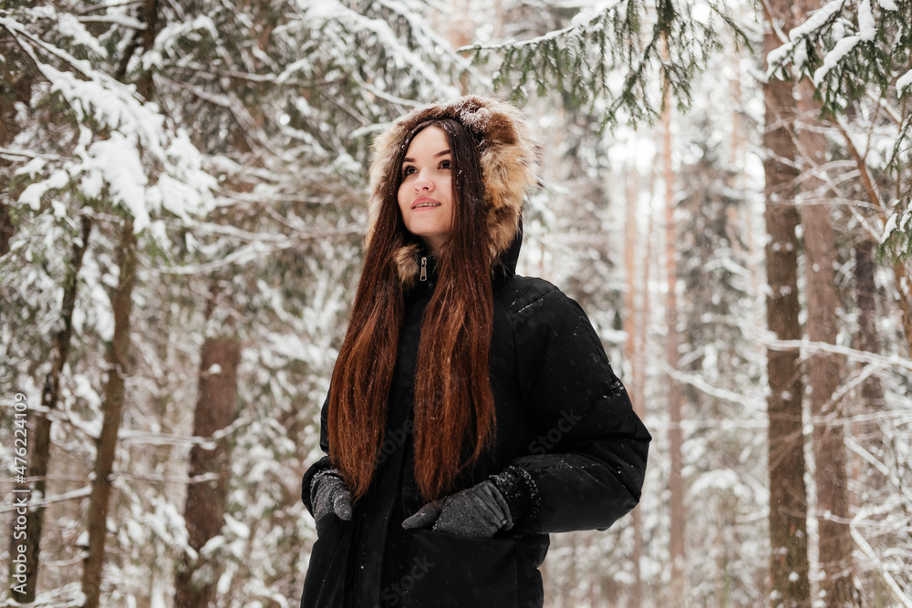Girl in coat and gloves standing in winter forest. Young woman with long brown hair in park outdoors. Girl in coat and gloves standing in winter forest. Young woman with long brown hair in park outdoors.