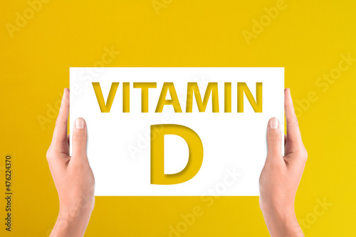 Vitamin D concept with hands holding the white paper on yellow background	 photo