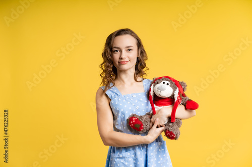 portrait of a beautiful girl in the studio. model in a blue dress with white polka dots plays with soft toys, has fun. yellow background. kindergarten teacher, nanny