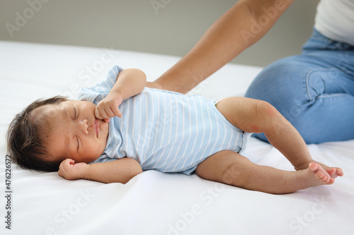 Adorable little sweet newborn baby girl sleeping on white bed with mother hand lightly touch her back, cute infant with mom in bedroom.