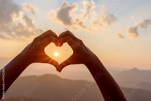 Hands in shape of love heart mountain sunset background.