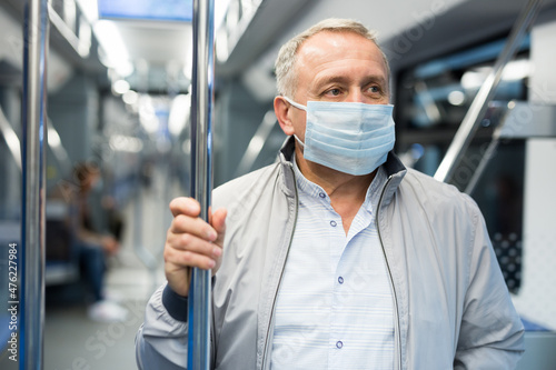 Mature passenger wearing protective mask rides in an underground metro car