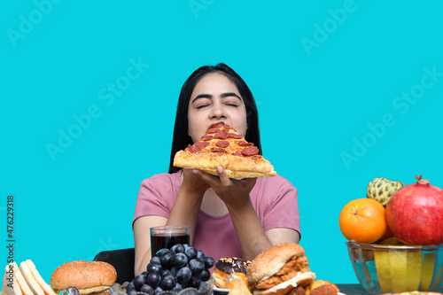 foodie girl sitting at fruit table eating pizza slice with colse eye indian pakistani model photo