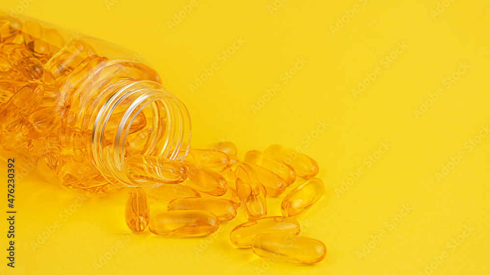 Soft gels of vitamin E and omega 3 spilled out of container on yellow background. Cpy space Soft gels of vitamin E and omega 3 spilled out of container on yellow background. Cpy space