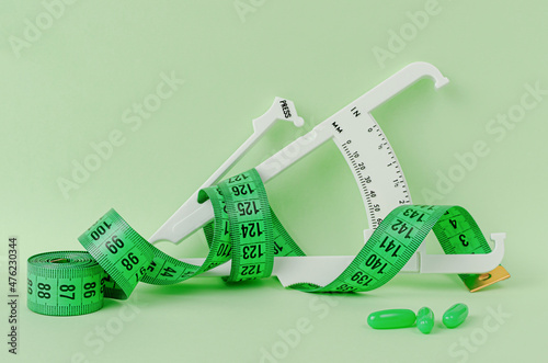 Slimming treatment concept. Measuring tape, supplement and caliper on green background.