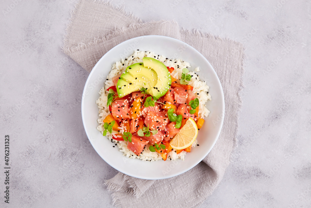 Poke bowl with salmon, rice, avocado, sesame seeds, micro greens, pepper and soy sauce on grey backround. Hawaiian diet food with fish. Top view. Flat lay. Close-up Poke bowl with salmon, rice, avocado, sesame seeds, micro greens, pepper and soy sauce on grey backround. Hawaiian diet food with fish. Top view. Flat lay. Close-up