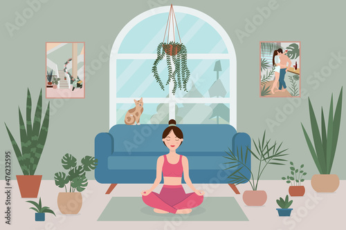 A woman practices yoga in a lotus position in a cozy room with a large window, potted plants and a cat.