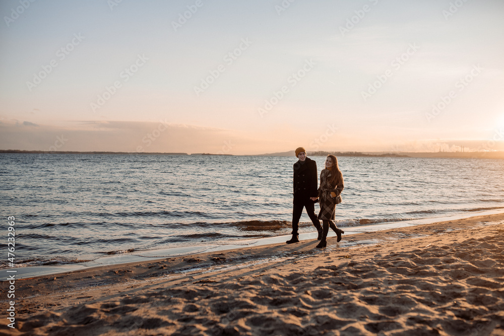 Naklejka premium Young beautiful couple on a walk by the sea in autumn in the off-season, hugging, walking, smiling
