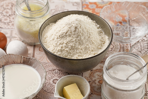 Baking ingredients for dough - white flour, eggs, milk, yeast, sugar, salt - on blue surface