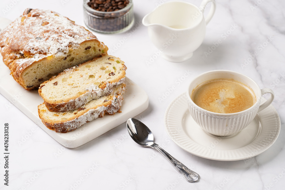 White porcelain cup with coffee cappuccino on a white saucer plate and christmas pastry stollen on a marble table White porcelain cup with coffee cappuccino on a white saucer plate and christmas pastry stollen on a marble table