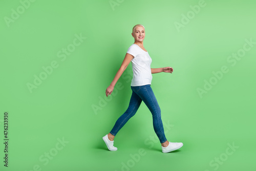 Full length profile side photo of mature pretty lady go walk casual outfit isolated over green color background