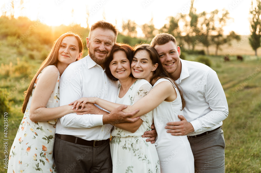 a family of different ages hugs tightly being in nature at sunset. family with five people happy together. portrait of a middle aged family. a group of people a family of different ages hugs tightly being in nature at sunset. family with five people happy together. portrait of a middle aged family. a group of people