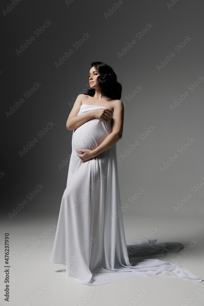 Caucasian young beautiful pregnant woman with dark hair in white fluttering fabric posing on a white background. isolates the banner space for text. Antique style