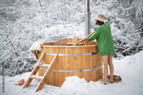 Foto Woman mixing hot water in outdoor wooden bath, preparing for hot water treatments while resting at snowy mountains