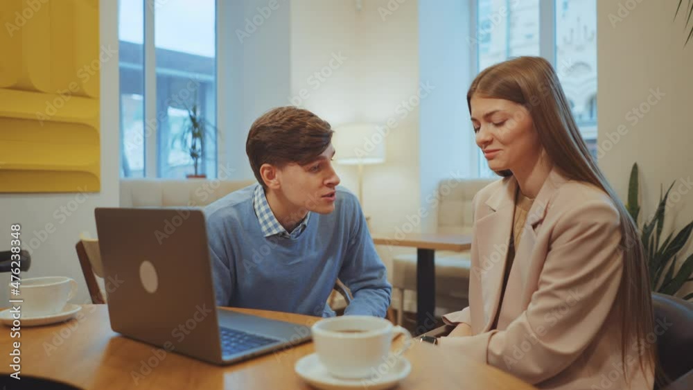 Young couple quarrelling in cafe, people having crisis in relationship. Man and woman sitting at table with cups and laptop, he talking emotionally and gesturing, she staying silent. Concept of stress