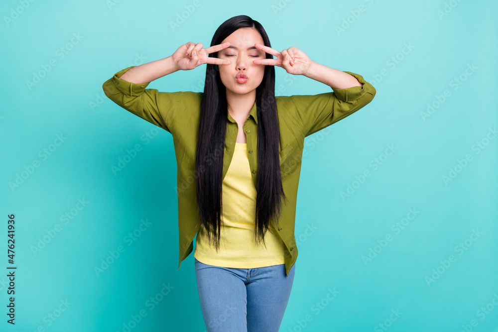 Photo of young attractive asian girl pouted lips show peace cool v-sign isolated over turquoise color background Photo of young attractive asian girl pouted lips show peace cool v-sign isolated over turquoise color background