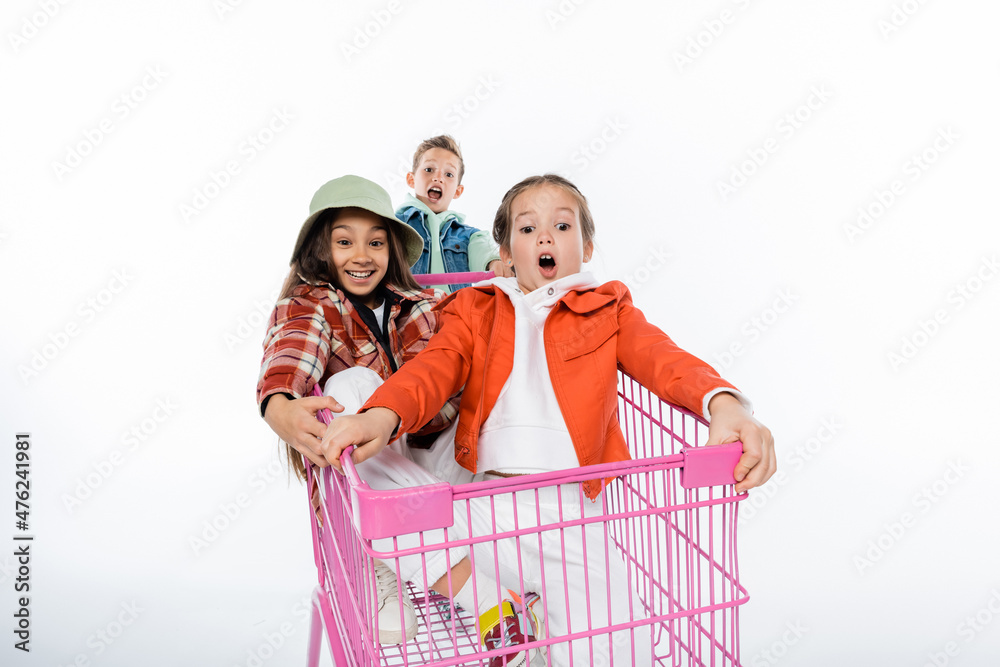 joyful kids riding in pink shopping cart on white.