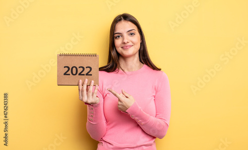 pretty woman smiling cheerfully, feeling happy and pointing to the side. 2022 calendar concept photo