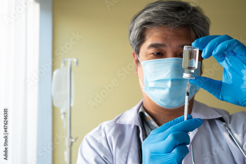 An Asian male doctor wears a medical glove and face mask holding syringe taking covid 19 coronavirus vaccine to study and analyze antibody samples for the patient. Concept of diseases, medical care