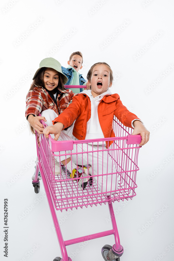 cheerful kids riding in pink shopping cart isolated on white. cheerful kids riding in pink shopping cart isolated on white.