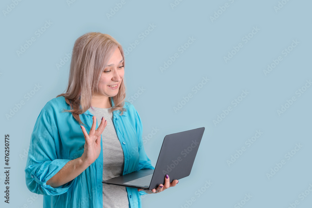 An adult blonde woman 35-40 years old communicates via video link holding a modern laptop in her hands and waving her hand towards the laptop screen. An adult blonde woman 35-40 years old communicates via video link holding a modern laptop in her hands and waving her hand towards the laptop screen.