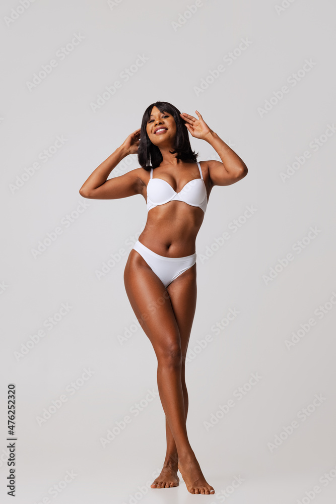 Full-length portrait of young beautiful slim girl in white underwear posing isolated over gray studio background. Natural beauty concept. Full-length portrait of young beautiful slim girl in white underwear posing isolated over gray studio background. Natural beauty concept.