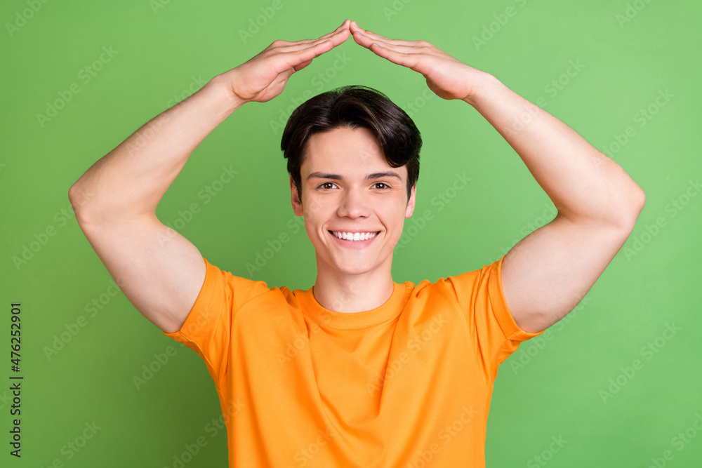 Photo of positive happy young man hold hands above head roof house isolated on green color background Photo of positive happy young man hold hands above head roof house isolated on green color background