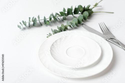 Spring elegant table setting, Rustic restaurant menu concept. white dishes and silverware next to eucaliptus branches on a table. mock up for meal placement